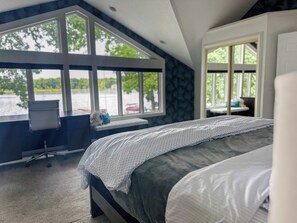 A bedroom with a large bed, a desk, and a view of a lake through large windows.