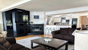 A modern living room with a fireplace, dark brown sofas, a coffee table, and a kitchen area in the background. - Wolf Lake Haven - Lakefront Sleeps 16 (Jackson)