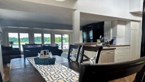 A dining area with a table set for four, a kitchen in the background, and a view of the outdoors. - Wolf Lake Haven - Lakefront Sleeps 16 (Jackson)
