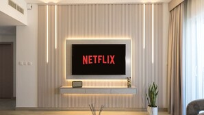 A modern living room with a flat-screen TV mounted on a wall, a small shelf with a decorative item, and a potted plant. - 1BDR Premium Yas Island - Ferrari, Sea World, F1 (Abu Dhabi)