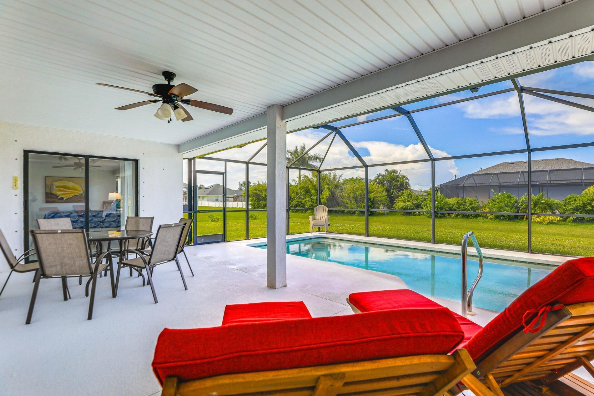 A pool area with a glass enclosure, a ceiling fan, and a view of a residential neighborhood.