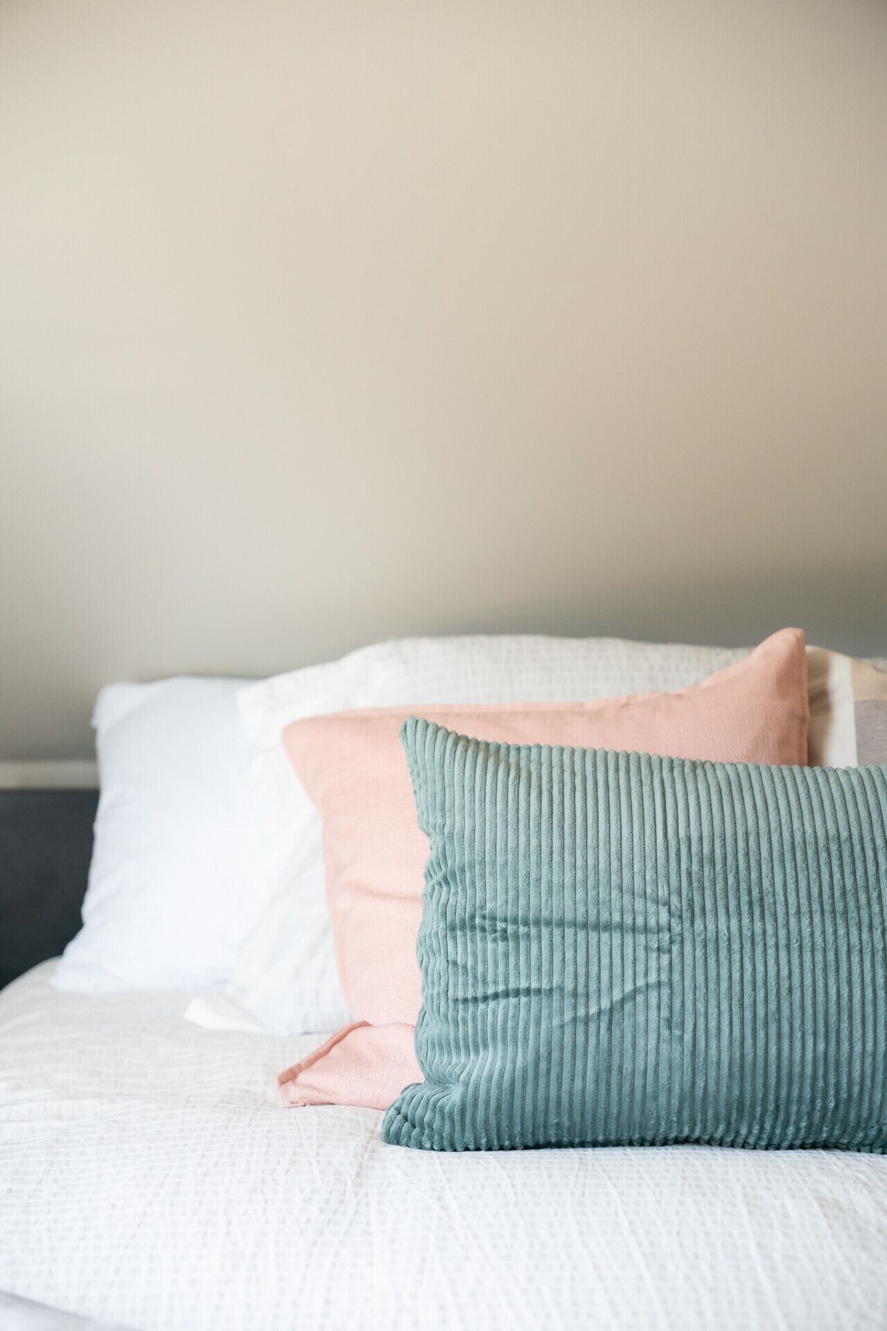 Un lit avec une literie blanche et trois oreillers de couleurs différentes.