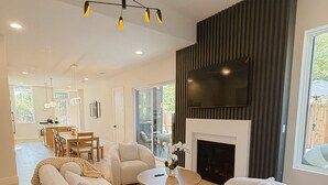 A spacious living room with a fireplace, modern furniture, and a large TV mounted on the wall.