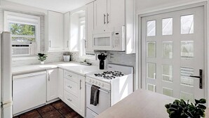 A modern kitchen with white cabinetry, a gas stove, a microwave, and a window providing natural light. - Cozy 2BR Getaway in Lake Worth Beach – Walk to the Ocean! (Lake Worth Beach)