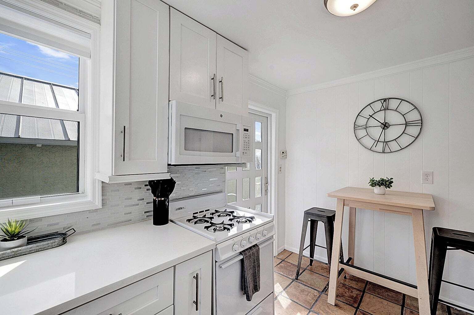 Una cocina moderna con armarios blancos, microondas integrado, cocina a gas y un reloj de pared.