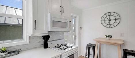 Una cocina moderna con armarios blancos, microondas integrado, cocina a gas y un reloj de pared.