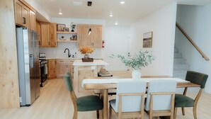 Una cocina moderna con armarios de madera, un refrigerador de acero inoxidable, una mesa de comedor con sillas y una escalera.