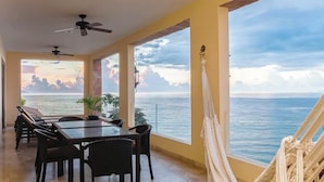 A dining area with a view of the sea, a hammock, and ceiling fans.