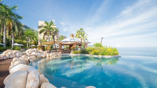 A resort pool with a clear view of the ocean, surrounded by palm trees and a gazebo.
