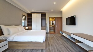 Et moderne hotelværelse med en stor seng, fjernsyn, walk-in closet og badeværelse.