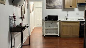A modern kitchen with wooden cabinets, a microwave, and a sink. There is a TV mounted on the wall and a small table with decorative items.