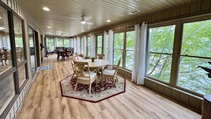Amplia habitación con un gran comedor rodeado de sillas, ventanas grandes que ofrecen vistas a la vegetación y suelo de madera.
