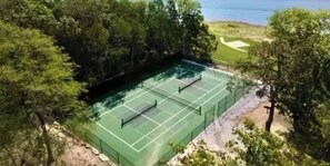 An outdoor tennis court surrounded by trees and a body of water.