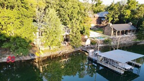 Un barco amarrado con una zona de estar techada, una pequeña construcción con cimientos de piedra y una casa con techo de metal.