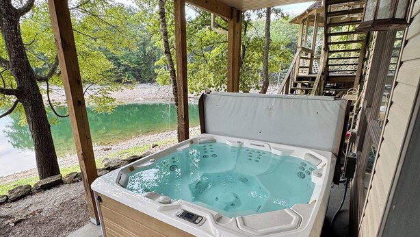 Un jacuzzi con revestimiento de madera y panel de control, situado en un área techada con ventilador de techo y vista a un lago.