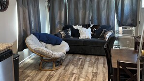 En stue med en mørk sofa, en gyngestol og et spisebord med stole.