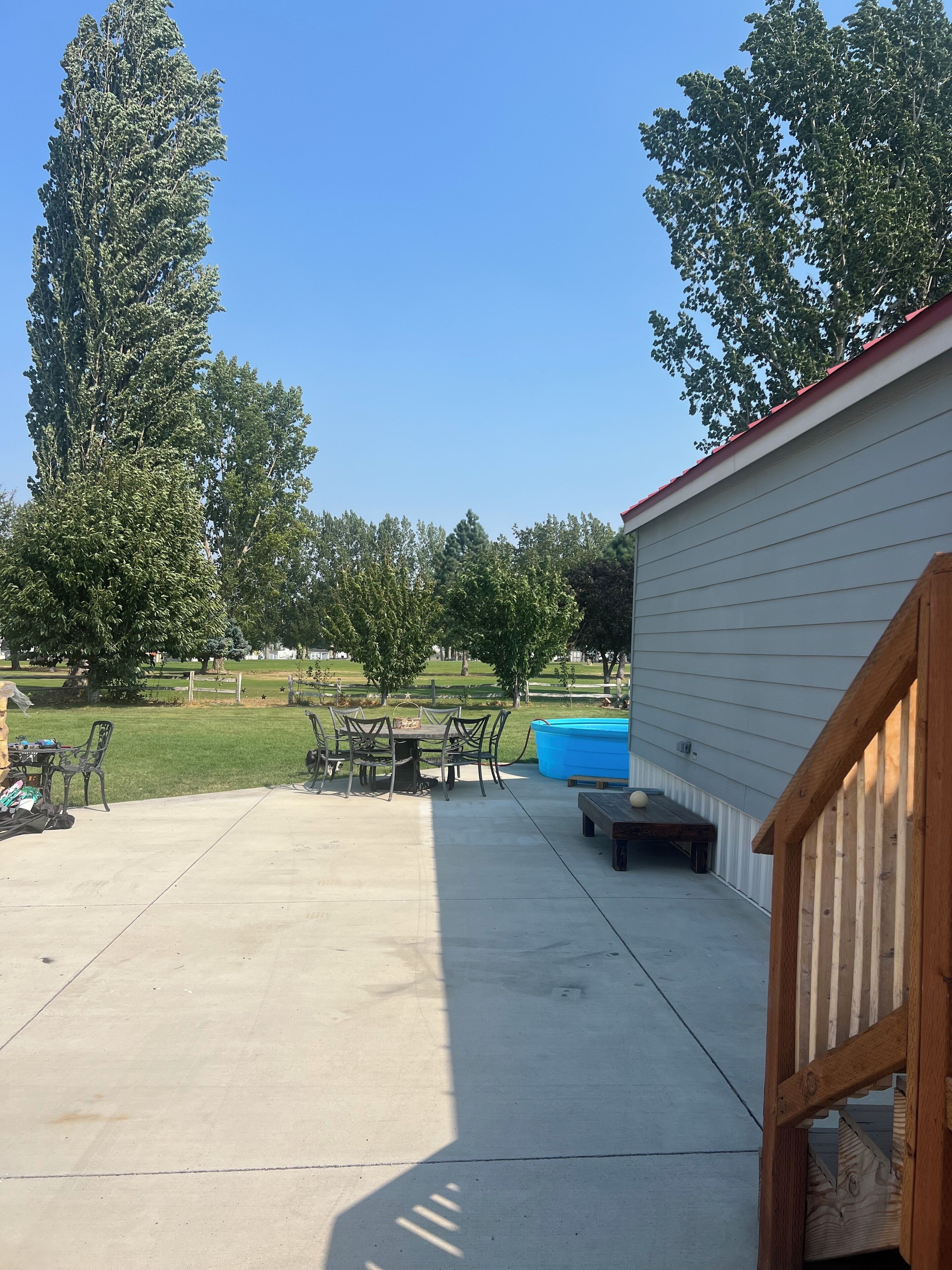 A backyard with a concrete patio, a pool, and a wooden deck.