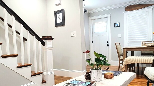 A living room with a white coffee table, a brown leather sofa, a striped rug, and a staircase with white railings.