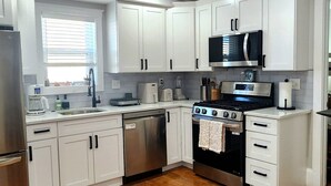 A modern kitchen with white cabinets, stainless steel appliances, and a wooden floor.