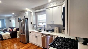A modern kitchen with stainless steel appliances, white cabinetry, and a wooden floor.