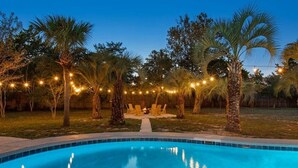 Ein Pool, umgeben von Palmen und Lichterketten, mit einem Weg zu einer Sitzgruppe.