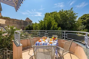 An outdoor dining area with a table set for breakfast, surrounded by metal railings and greenery.