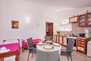 Habitación de hotel compacta con comedor, kitchenette y cama con ropa de cama rosa.