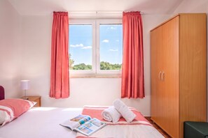 Un dormitorio con cama, armario de madera, ventana con cortinas y una revista sobre la cama.