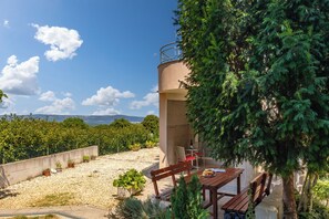 Une terrasse avec une table et des chaises en bois, entourée de plantes en pot et offrant une vue sur la mer.