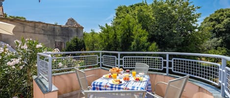 An outdoor dining area with a table set for breakfast, surrounded by metal chairs and a railing.