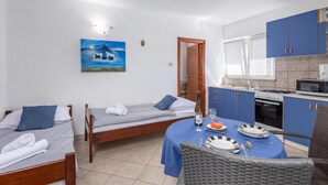 Een compacte hotelkamer met twee eenpersoonsbedden, een zithoek met een tafel voor twee personen, een kitchenette en een schilderij aan de wand.