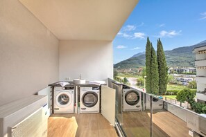 A balcony with three washing machines, a sink, and a view of a mountainous landscape. - Sole E Lago, Riva del Garda, Italy (Riva del Garda)