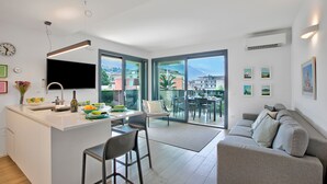 Cozinha moderna com uma ilha central, área de refeições com mesa de vidro e um sofá na sala com vista para a cidade.