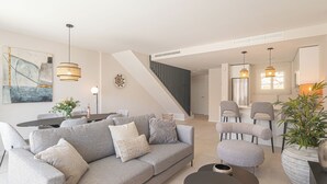 A modern living room with a grey sofa, a dining table, and a staircase leading to another level.