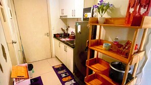 A compact kitchen with white cabinets, a refrigerator, and a wooden shelf with kitchen items. - Cosy Condo with Balcony at Makati SM Jazz (Makati City)
