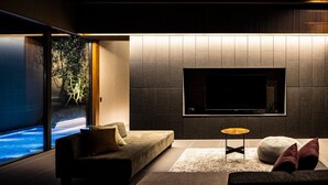 A modern living room with a large flat-screen TV mounted on the wall, a sofa, a small round table, and a view of a pool through large windows. - A private villa where you can step away from your daily life and savor "extra... (karatushi watada honmura)