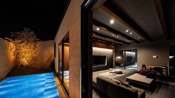 A modern indoor pool area with a glass enclosure, a seating area with sofas and a table, and a visible outdoor tree. - A private villa where you can step away from your daily life and savor "extra... (karatushi watada honmura)