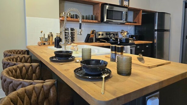 A modern kitchen with a wooden island, stainless steel appliances, and a variety of utensils and cookware.