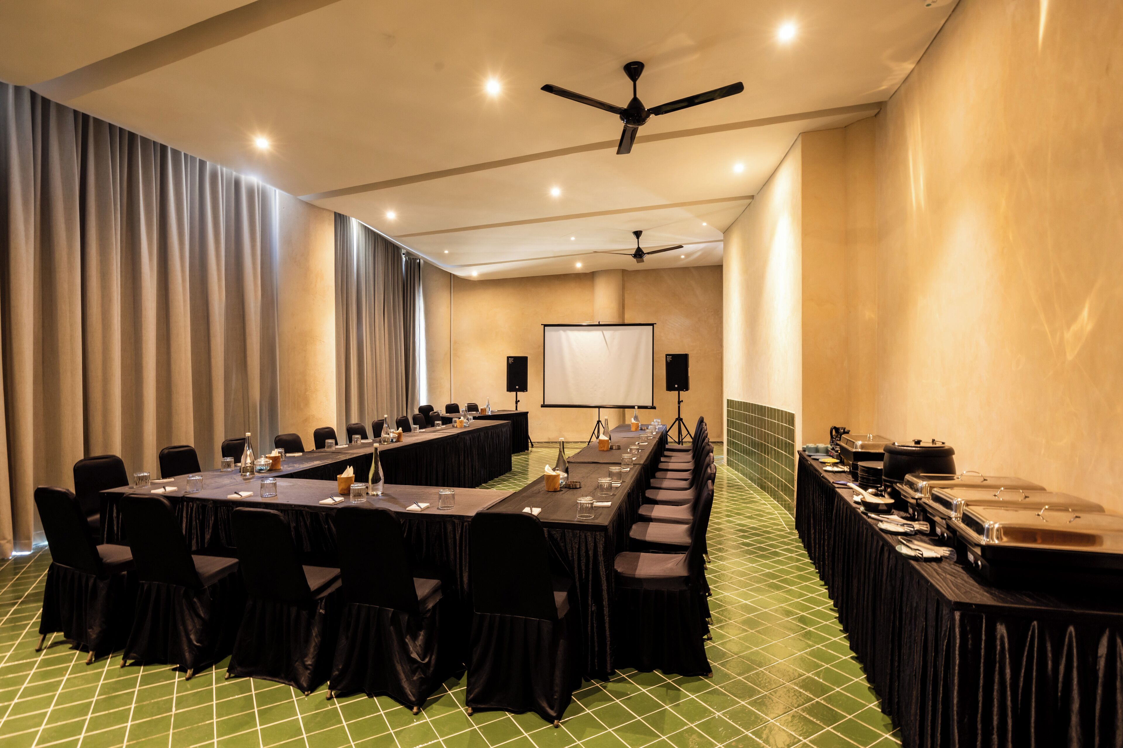 A conference room with a long table, chairs, a projector screen, and a buffet area.