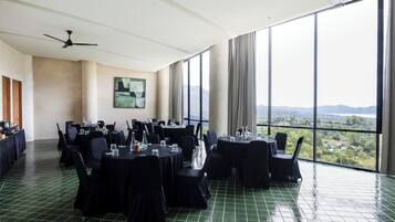 Un salón de conferencias con mesas redondas, sillas negras y un amplio ventanal con vistas a un paisaje montañoso.