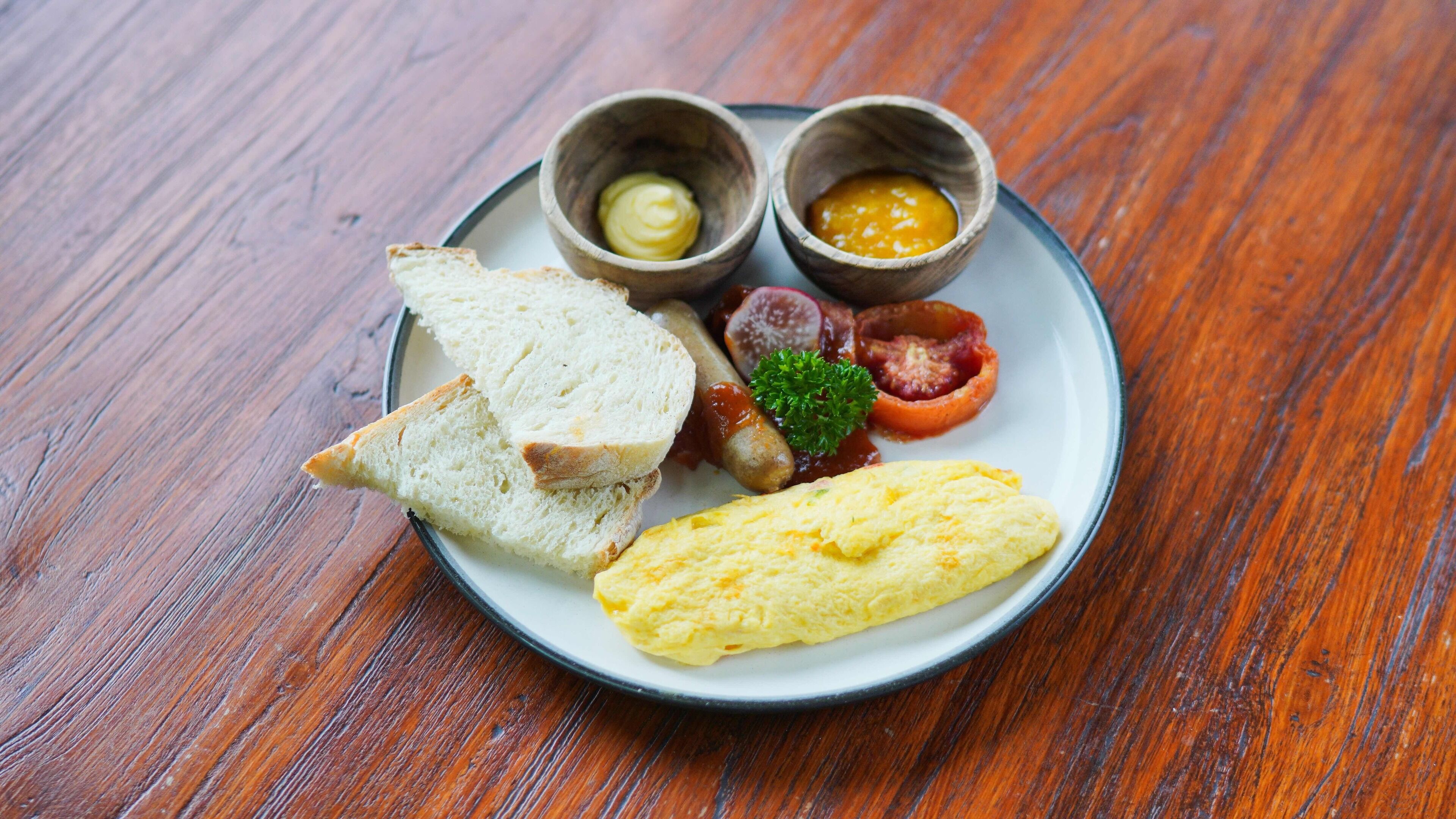 A plate with toast, scrambled eggs, sausages, and two small bowls of condiments.