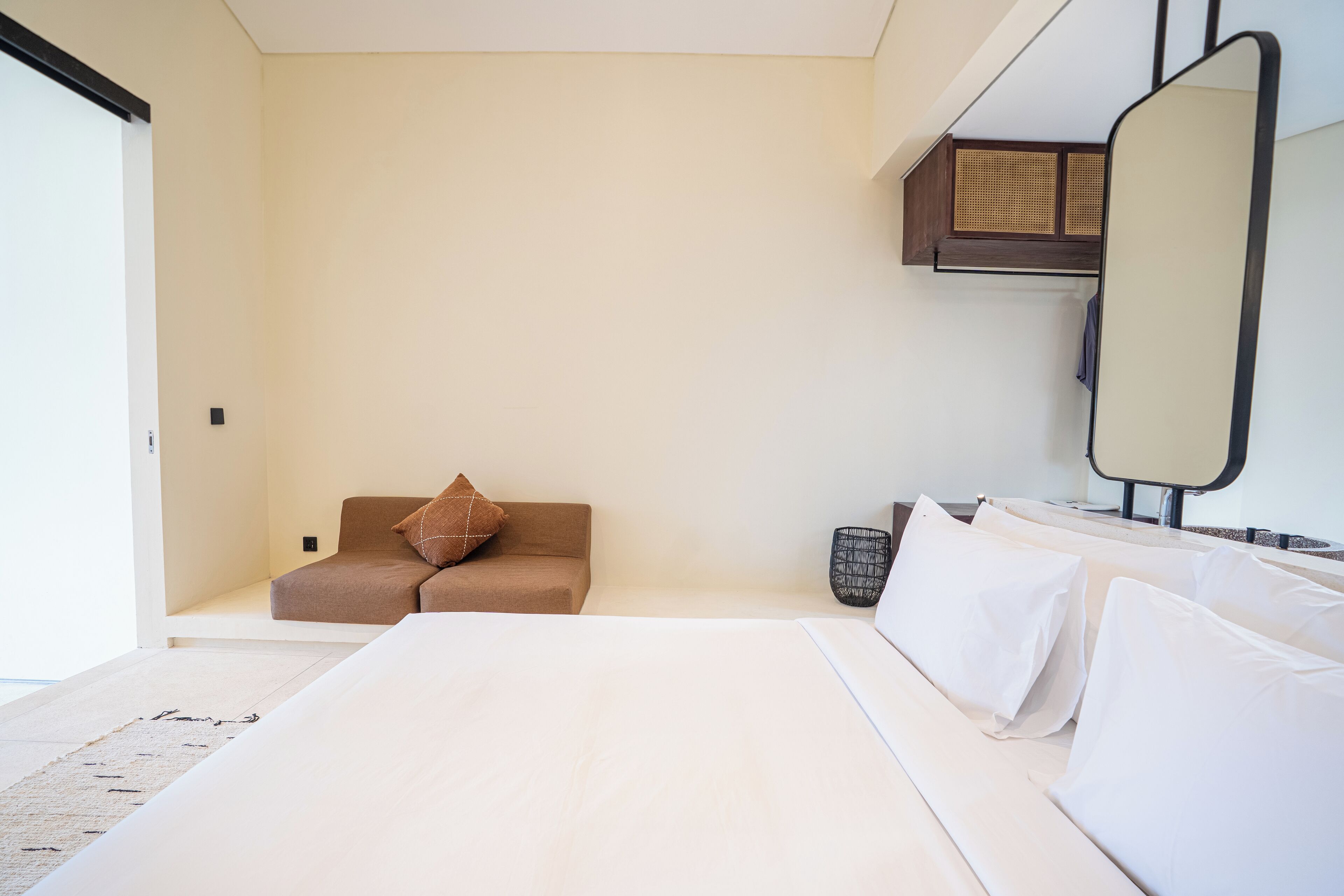 A modern hotel room with a large bed, a sofa, a small seating area, and a mirror.