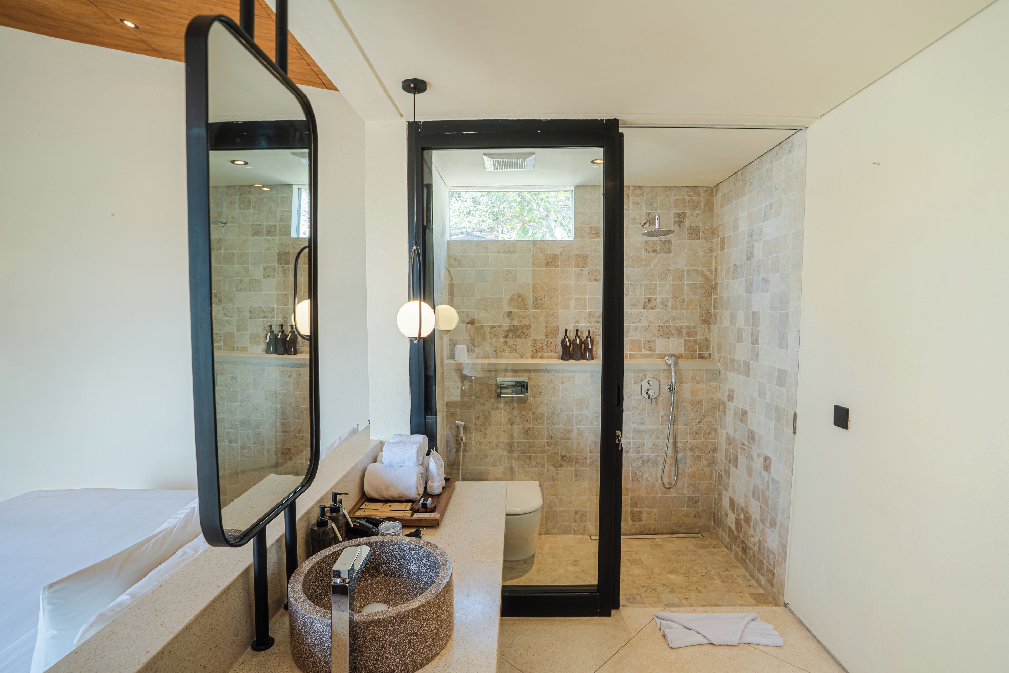Une salle de bain moderne avec une baignoire, un grand miroir, un lavabo rond et une douche séparée par une paroi de verre.