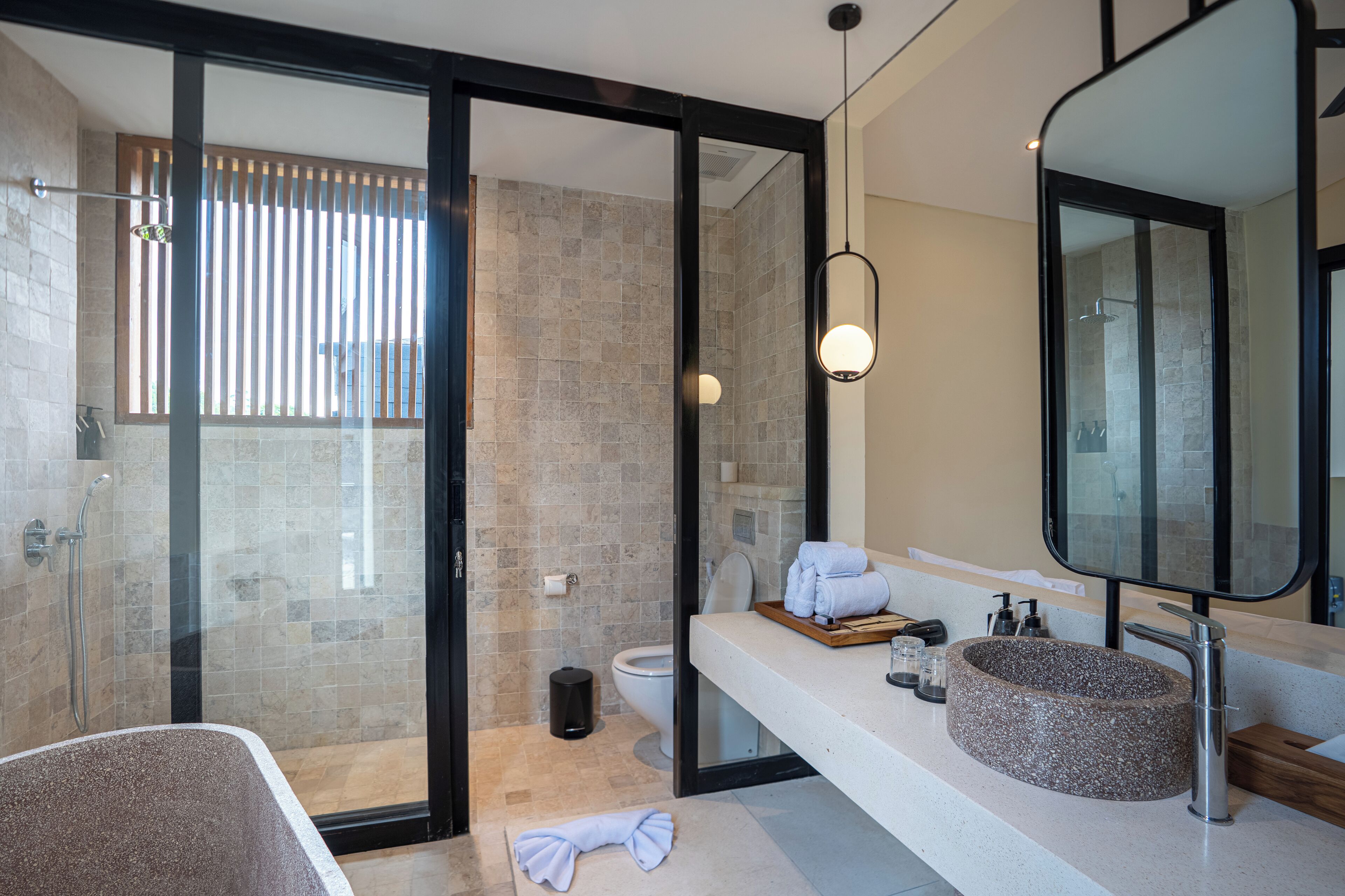 A modern bathroom with a glass-enclosed shower, a round stone sink, and a large mirror.