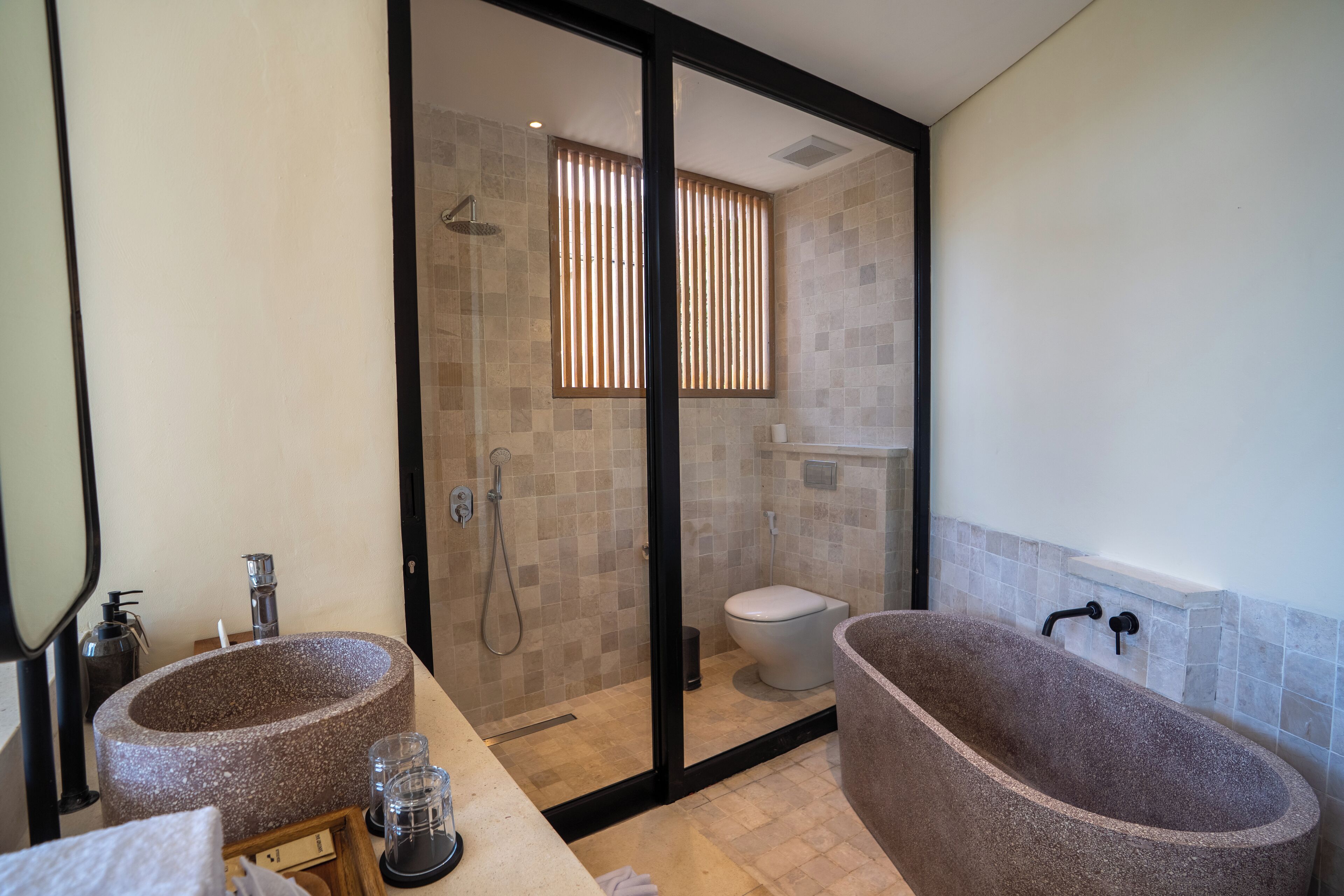 A bathroom with two freestanding stone sinks, a glass-enclosed shower, and a bathtub.