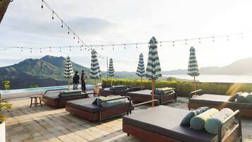 Terraço no telhado com área de estar ao ar livre, luzes de corda e vista para montanhas e um lago.