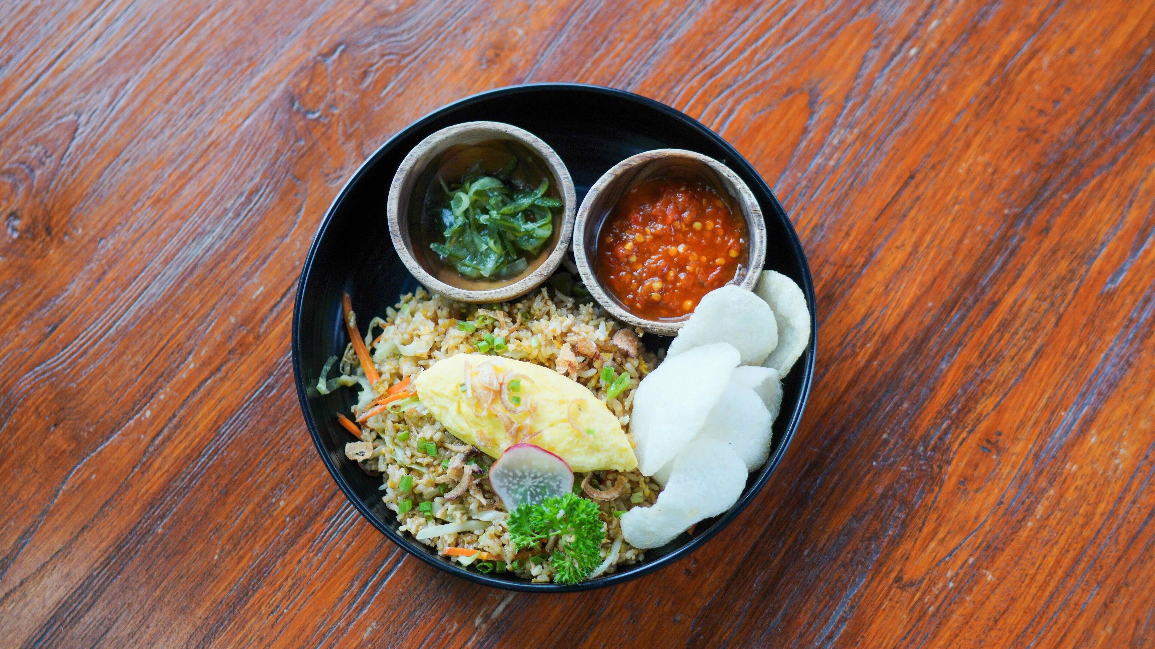 A bowl of fried rice with vegetables, an egg, and slices of radish on a wooden table.