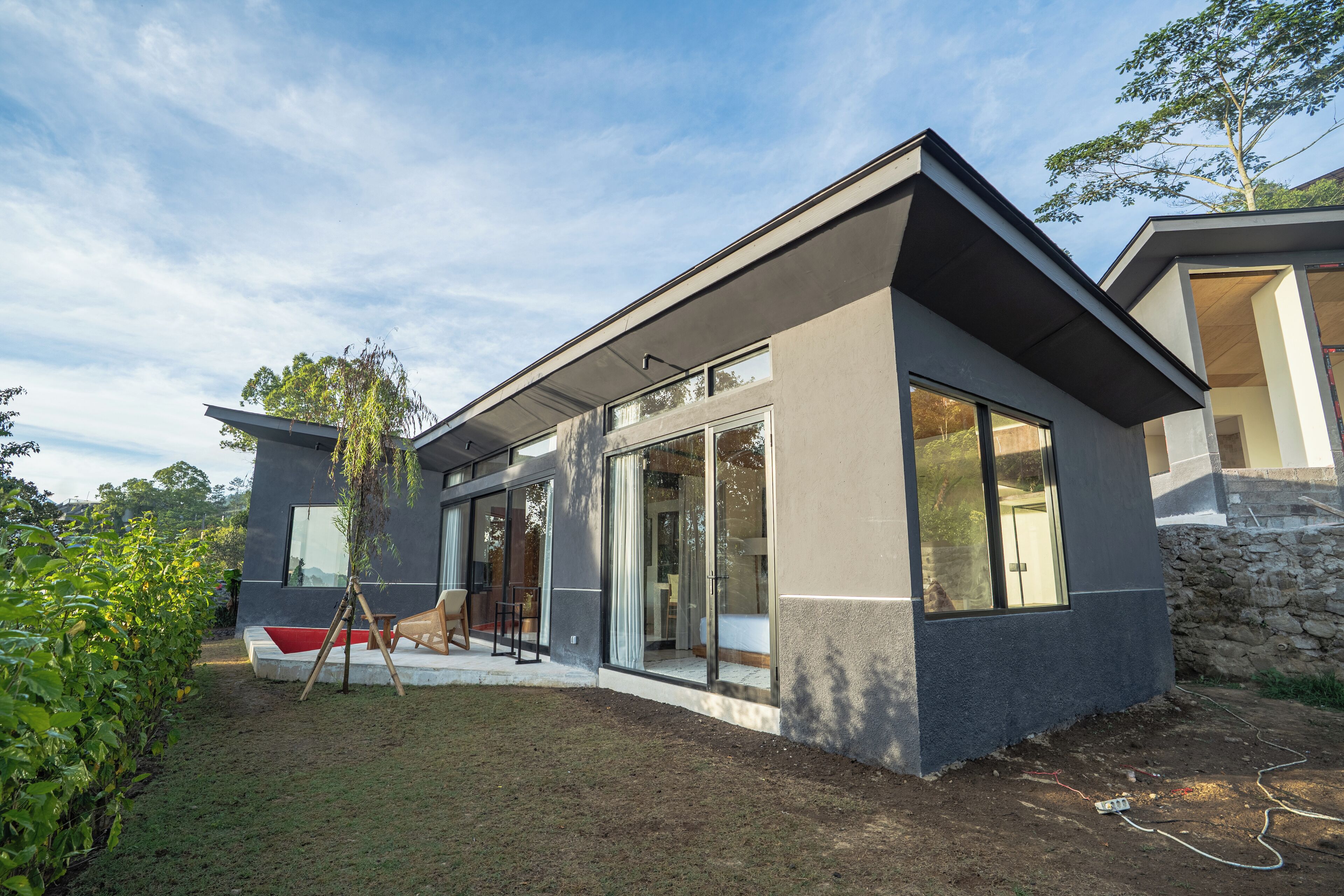 A modern house with large glass windows, a stone wall, and a grassy yard.