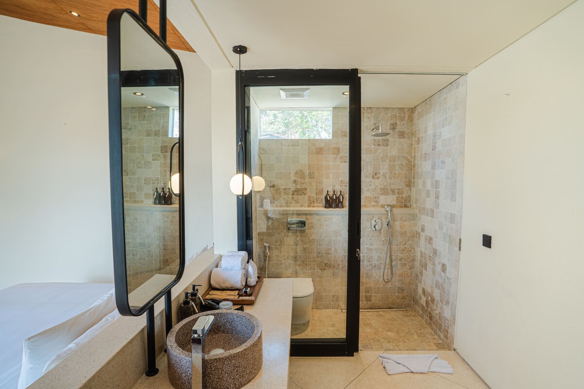 A modern bathroom with a bathtub, a large mirror, a round sink, and a shower area.