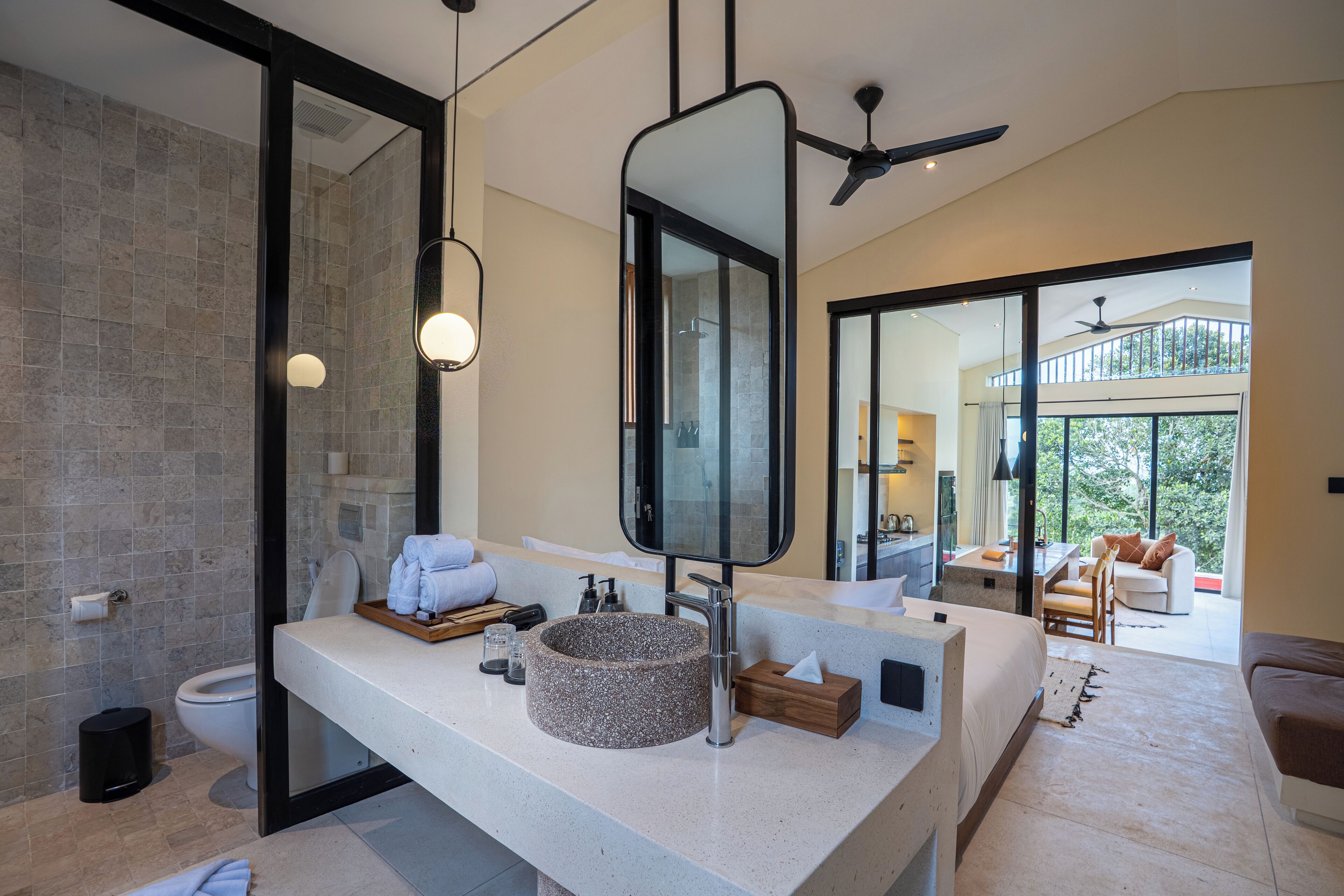 A modern bathroom with a large mirror, a round sink, and a toilet. There is a balcony with a view of the outdoors.